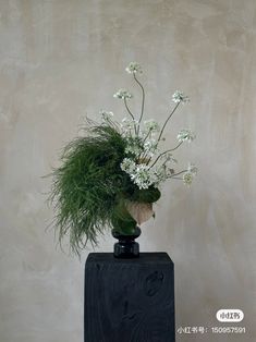 a black vase with white flowers and greenery in it sitting on a wooden block