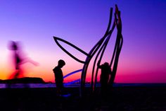 two people standing next to each other in front of the ocean at sunset or dawn