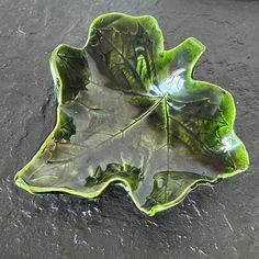 a green leaf shaped bowl sitting on top of a cement floor next to a puddle