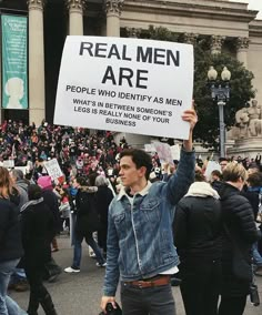 a man holding up a sign that says real men are people who identify as men