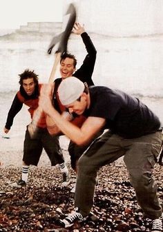 three men playing baseball on the beach with one holding an object in his hand and another reaching for it