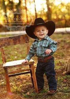 a little boy wearing a cowboy hat standing next to a wooden chair