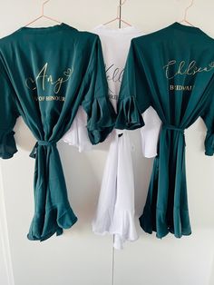 two green robes hanging on a wall with name written on the front and back of them