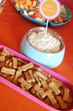 a table filled with bowls and trays of crackers on top of an orange table cloth