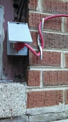 an electrical outlet on the side of a brick wall with red wires attached to it