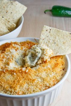 a white bowl filled with cheese and crackers on top of a table next to a green chili pepper