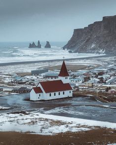 a small white church with a red roof near the ocean and cliffs in the background