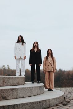 three women standing on top of steps in front of the camera, one wearing a white blazer