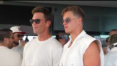 two men standing next to each other in front of a group of people wearing sunglasses