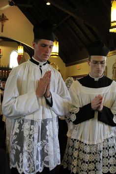 two men standing in front of each other wearing white and black clothing with hands folded