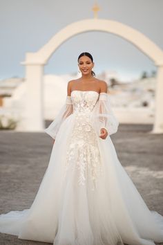 a woman in a white wedding dress posing for the camera with an arch behind her