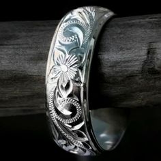 a wedding band with flowers and leaves engraved on the side, sitting on top of a piece of wood