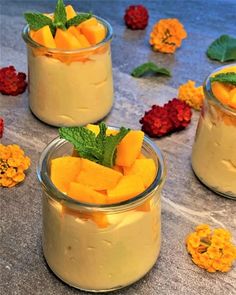 three jars filled with dessert sitting on top of a table next to flowers and leaves