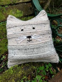 a knitted cat pillow sitting on top of a wooden bench