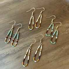 four pairs of earrings on a wooden table with beads and chains hanging from the earwires