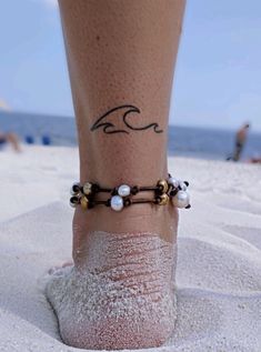 a woman's foot with a tattoo on it and pearls in the sand at the beach