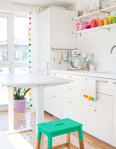 a kitchen with white cabinets and colorful accessories on the counter top, along with a green stool