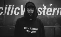 a man wearing a hoodie standing in front of a sign