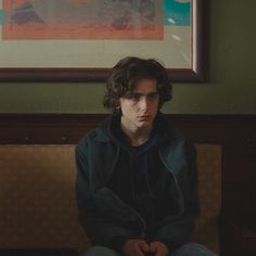 a young man sitting on top of a couch in front of a framed art piece