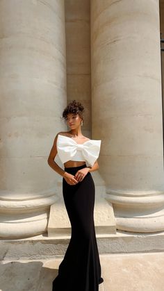 a woman in a black and white dress standing next to columns