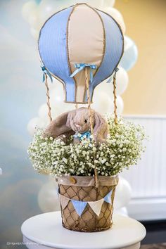 a stuffed animal in a basket with flowers and balloons on the table next to it