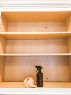 a brown spray bottle sitting on top of a wooden shelf next to a pink cloth