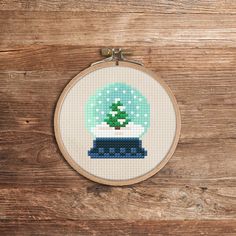 a cross stitch christmas ornament with a small green tree in it on a wooden surface