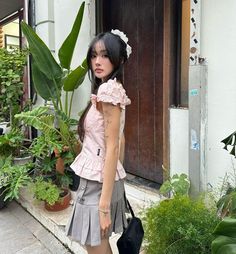 a woman standing in front of a door wearing a pink top and gray skirt with ruffles