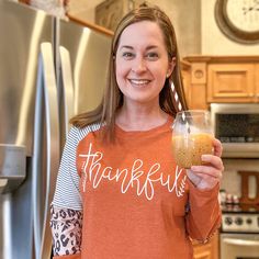 a woman holding a drink in her right hand and smiling at the camera while standing next to a refrigerator