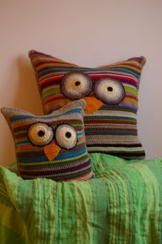 two crocheted owl pillows sitting on top of a green pillow case next to each other