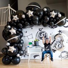 a young boy sitting on a chair in front of a wall with stars and balloons