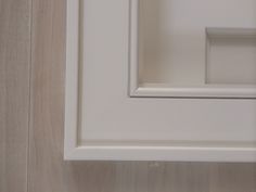 the corner of a white cabinet door with wood paneling on the wall behind it