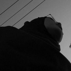 a person wearing a hood and sunglasses standing in front of power lines