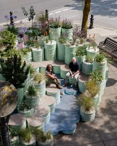 two people sitting on the ground in front of many potted plants and trees,