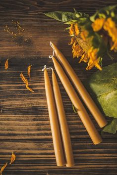 three candles sitting on top of a wooden table next to sunflowers and leaves