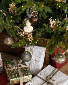 presents under a christmas tree with lights and ornaments on it's branches in front of a wicker basket