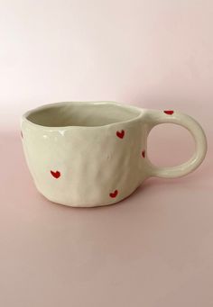 a white ceramic cup with red hearts on the outside and inside, sitting on a pink surface