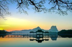 the sun is setting over a lake with benches on it and mountains in the background