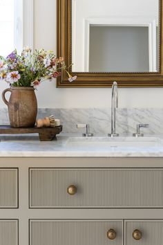 a bathroom vanity with marble counter top and gold framed mirror on the wall above it