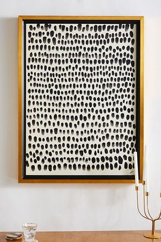 a white and gold framed artwork with black dots on it