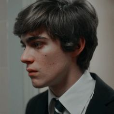 a young man in a suit and tie looks into the mirror while he is dressed up