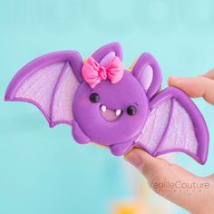 a hand holding a purple toy bat with a pink bow on it's head