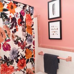 a bathroom with pink walls and floral shower curtain, toilet seat cover and framed pictures on the wall