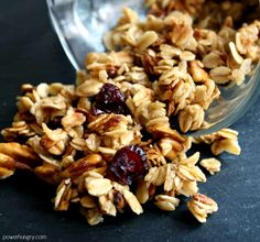 granola with cranberries and nuts in a glass bowl next to a spoon