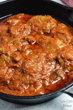 a skillet filled with meat and sauce on top of a table