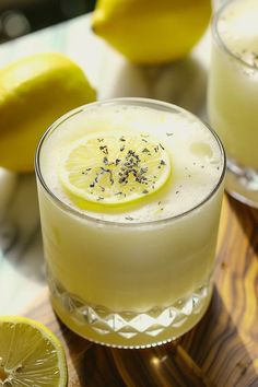 two glasses filled with lemonade sitting on top of a wooden table next to sliced lemons