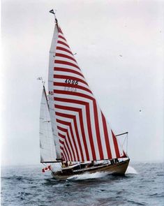 a sailboat with red and white stripes on it's sails in the ocean