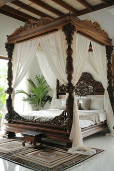 a canopy bed with white drapes on top of it in a room next to a potted plant