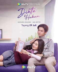 two people sitting on a purple couch with a book