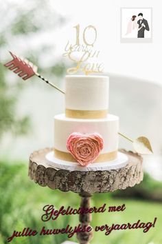 a three tiered wedding cake with an arrow and rose decoration on the top is sitting on a tree stump